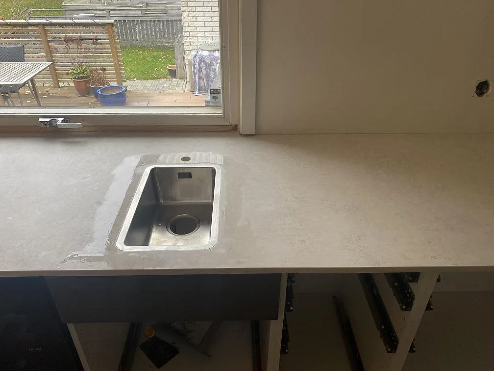 Köksbänkskiva i matt grå Dekton Lunar med underlimmad rostfri diskho och fönster mot trädgården i ett kök i Sävedalen.