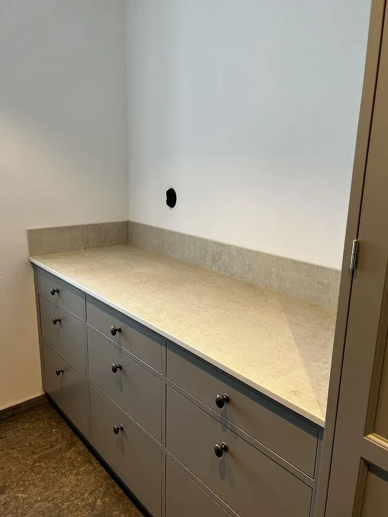 Stänkpanel och bänkskiva i Dekton Lunar, matt ljusgrå keramik, mot grå skåpsluckor i ett kök i Tygelsjö.