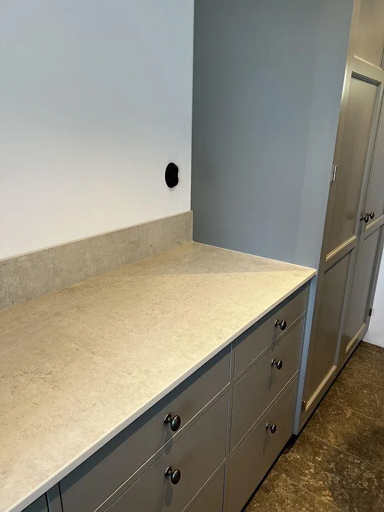 Dekton Lunar i matt gråvit keramik som bänkskiva och väggbeklädnad i ett kök under montering i Tygelsjö.