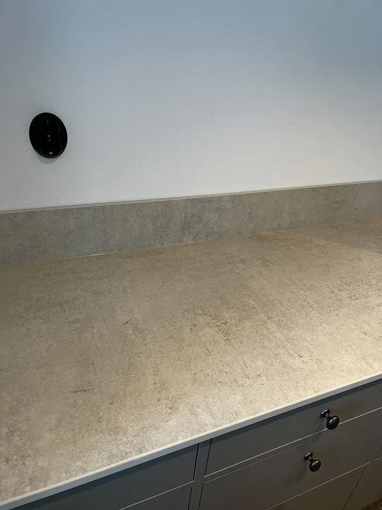 Närbild på Dekton Lunar stänkpanel i ljusgrå keramik mot grå köksluckor i ett kök i Tygelsjö.