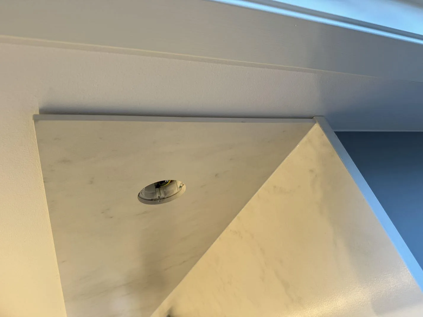 Hörnvy av matt Dekton Marina Kc Velvet som bänkskiva och väggskiva med runt uttagshål i ett kök i Jonstorp.