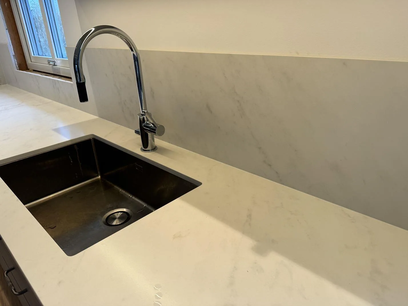 Detalj av köksbänkskiva i Dekton Marina Kc Velvet, matt keramik, vid diskho och stänkpanel under fönster i Jonstorp.