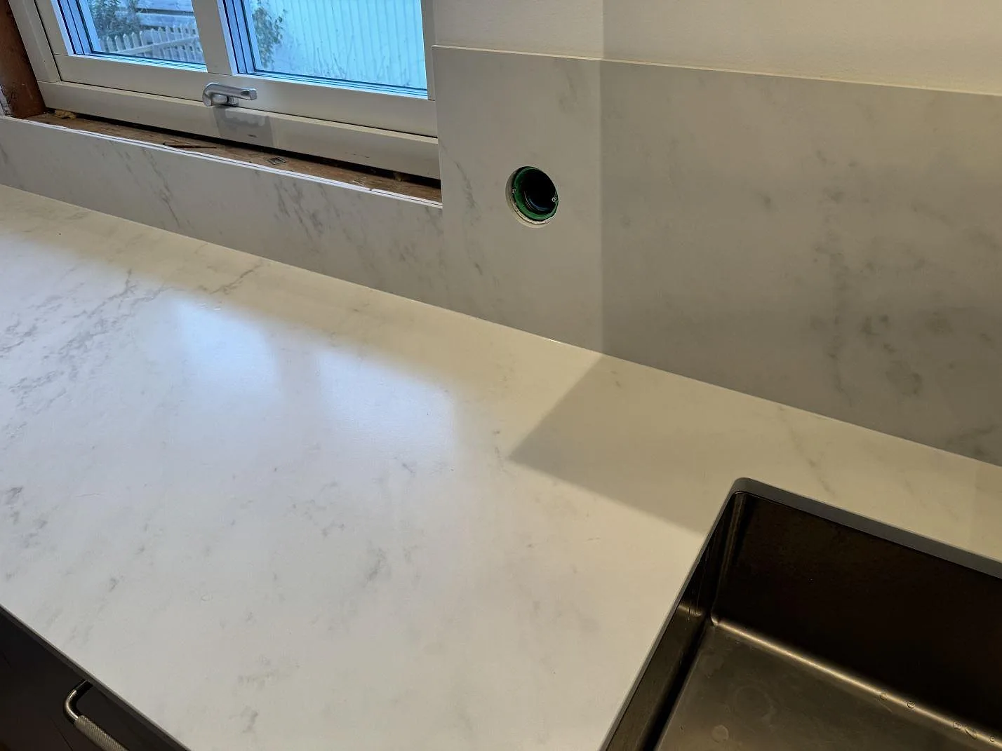 Ljus köksbänkskiva i matt Dekton Marina Kc Velvet med stänkpanel, fönsternisch och håltagning för eluttag i Jonstorp.