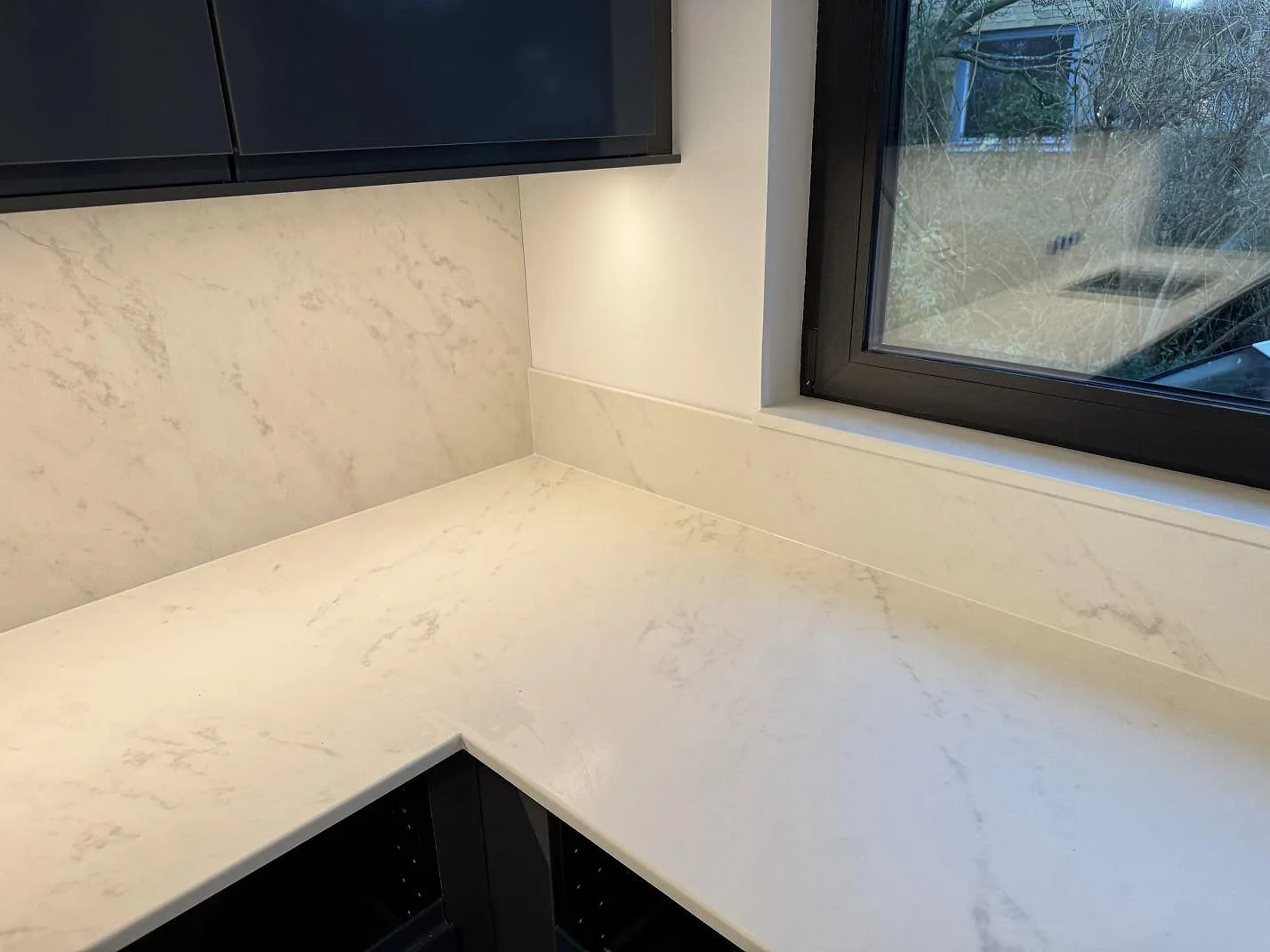 Hörn av matt Dekton Marina Kc Velvet med ljus ådring, lågt stänkskydd och svart fönsterkarm i ett kök i Lund.