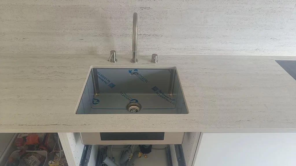 Installerad köksbänkskiva i matt Dekton Marmorio med mörk diskho, blandare och synlig öppen skåpsstomme i Halmstad.