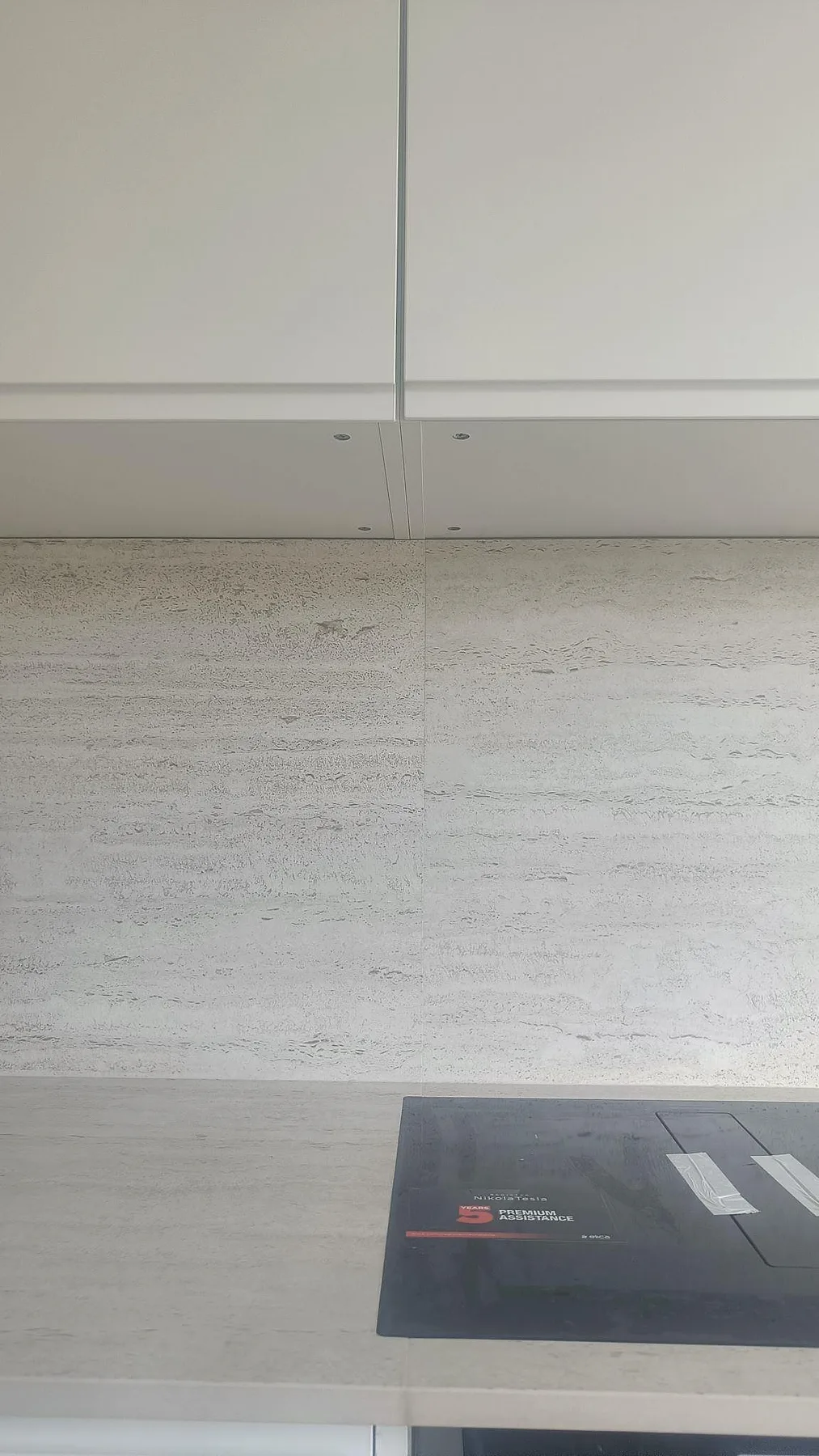 Porträttbild av matt Dekton Marmorio stänkskydd och bänkskiva med svart häll under vita överskåp i Halmstad.