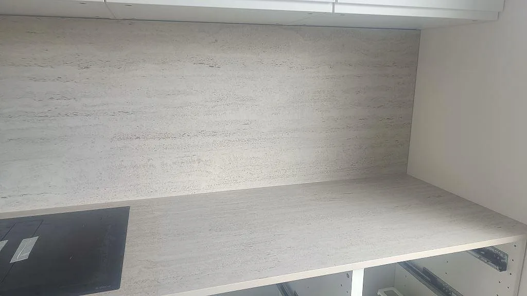 Rak arbetsyta i matt Dekton Marmorio med svart häll och matchande stänkskydd över öppna skåpsstommar i Halmstad.