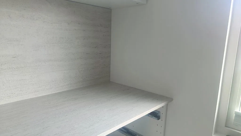 Hörnvy av matt Dekton Marmorio bänkskiva och stänkskydd vid fönster i ett ljust kök i Halmstad.