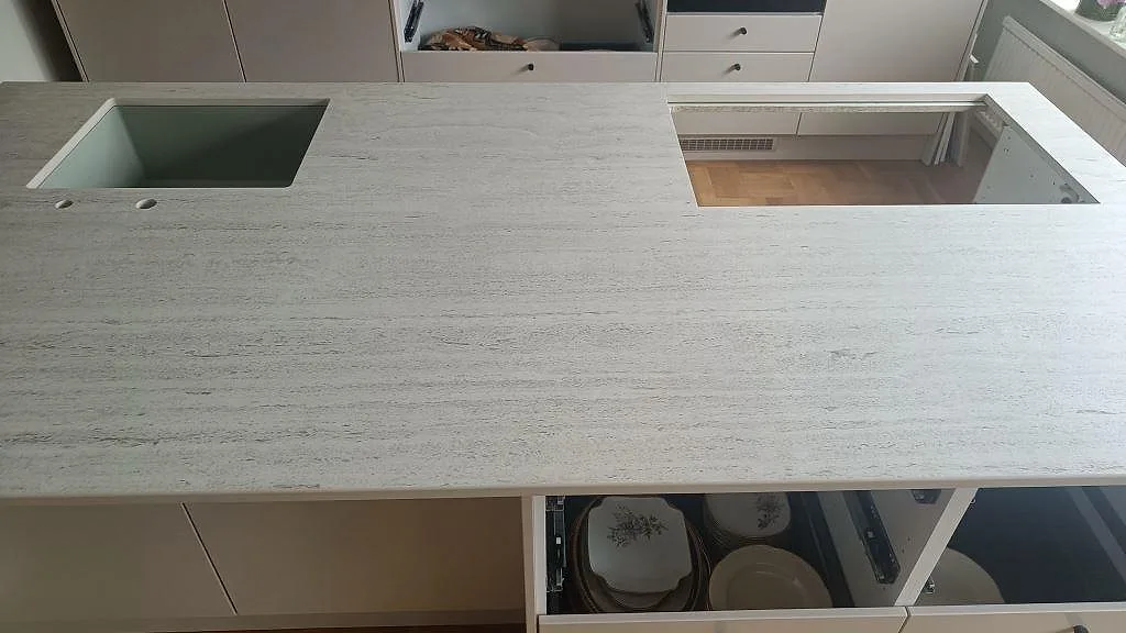 Bänkskiva i matt Dekton Marmorio med underlimmad diskho och hälluttag i en köksö under montering i Limhamn.
