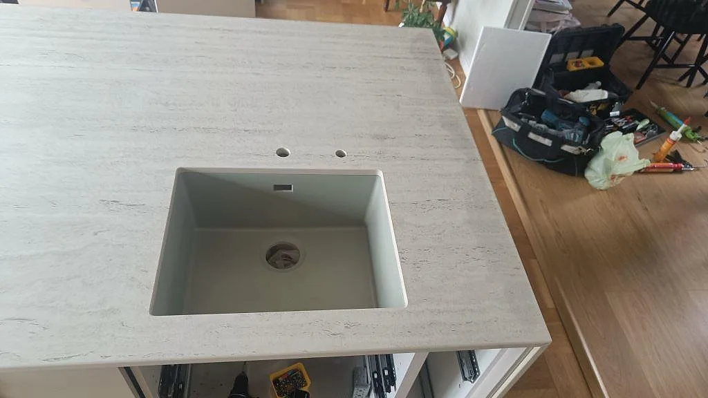 Detalj av underlimmad diskho i matt Dekton Marmorio på köksö i Limhamn, med monteringsverktyg i rummet.
