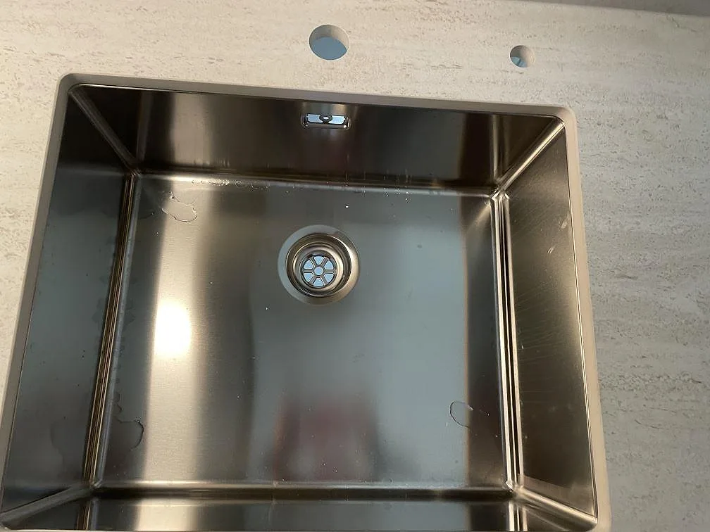 Detalj av underlimmad rostfri diskho i en köksbänkskiva av matt Dekton Marmorio keramik i Malmö.