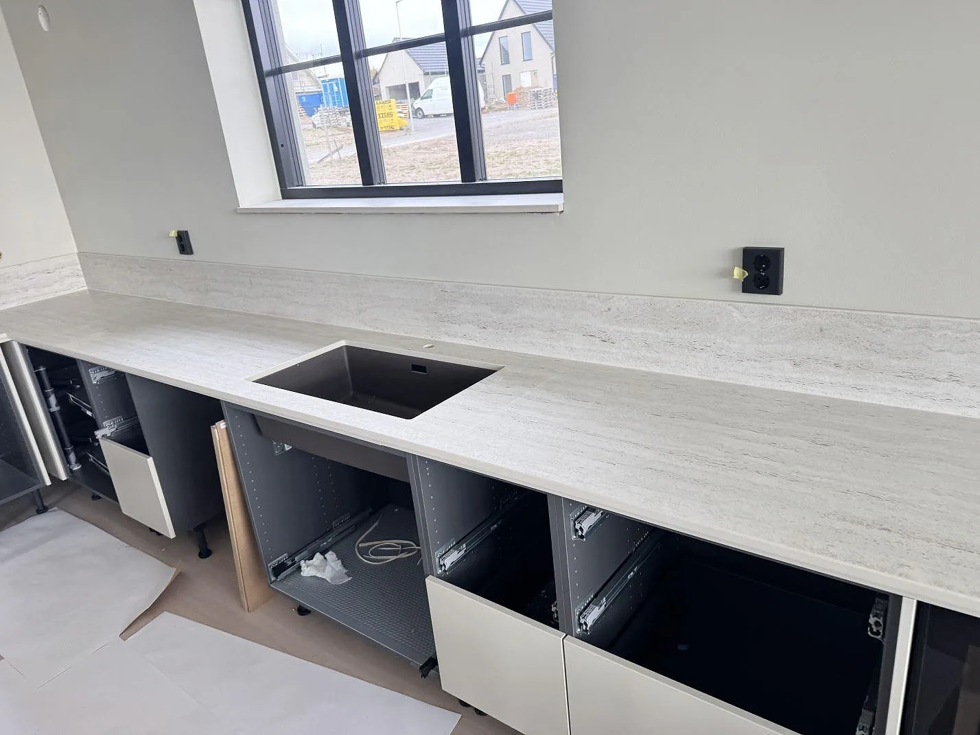 Lång köksbänkskiva i matt Dekton Marmorio med mörk diskho, 12 mm stänkkant och öppna stommar i ett kök i Skurup.