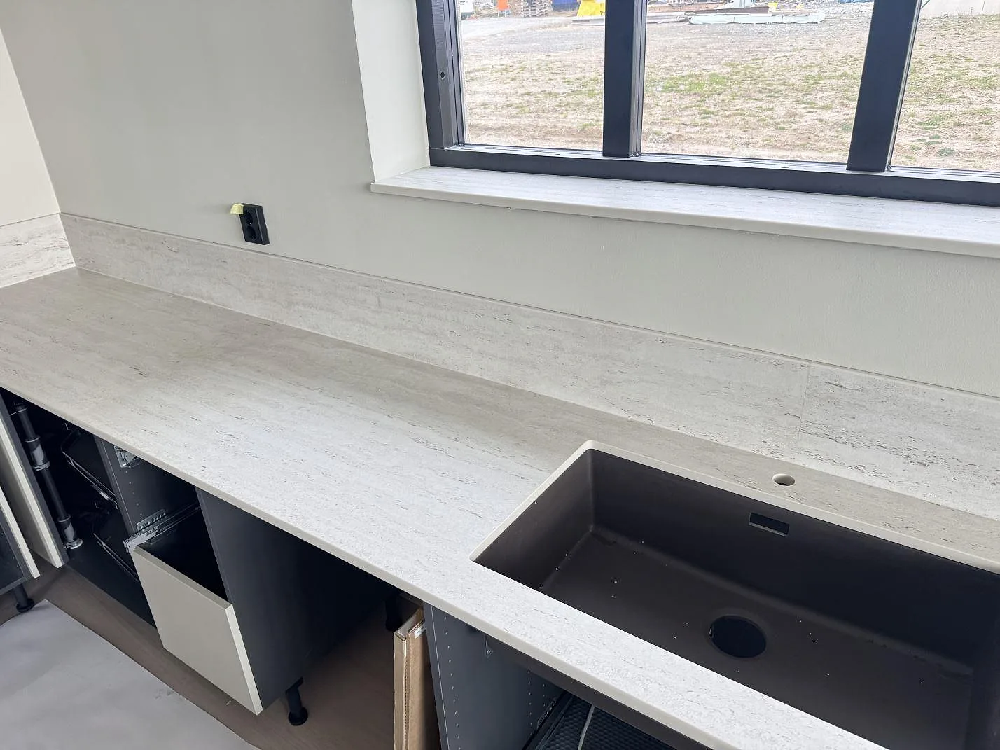 Matt Dekton Marmorio bänkskiva med mörk diskho vid fönster och uppvikt stänkkant i ett kök under montering i Skurup.