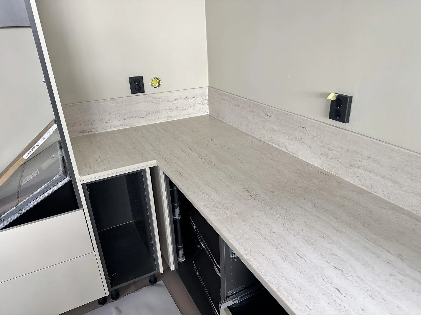 Hörnvy av matt Dekton Marmorio som köksbänkskiva med matchande låg stänkkant och ljusa luckor under montering i Skurup.