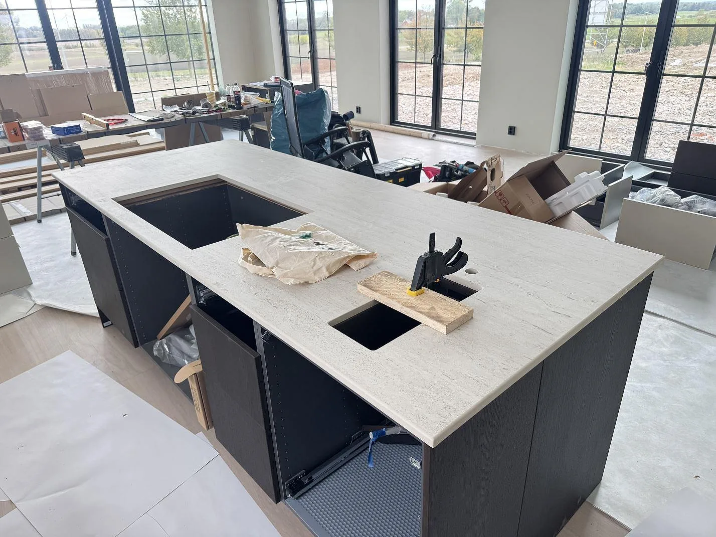 Köksö med matt bänkskiva i Dekton Marmorio keramik, förberedda urtag och öppna köksstommar under montering i Skurup.
