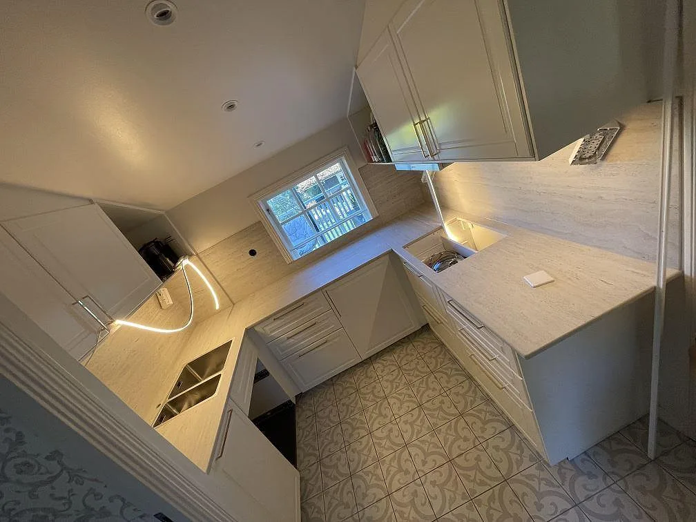 Köksbänkskiva i Dekton Marmorio, matt, i ett ljust U-format kök i Trosa, med matchande väggbeklädnad i samma keramik och vit köksinredning, fotograferat under montering.