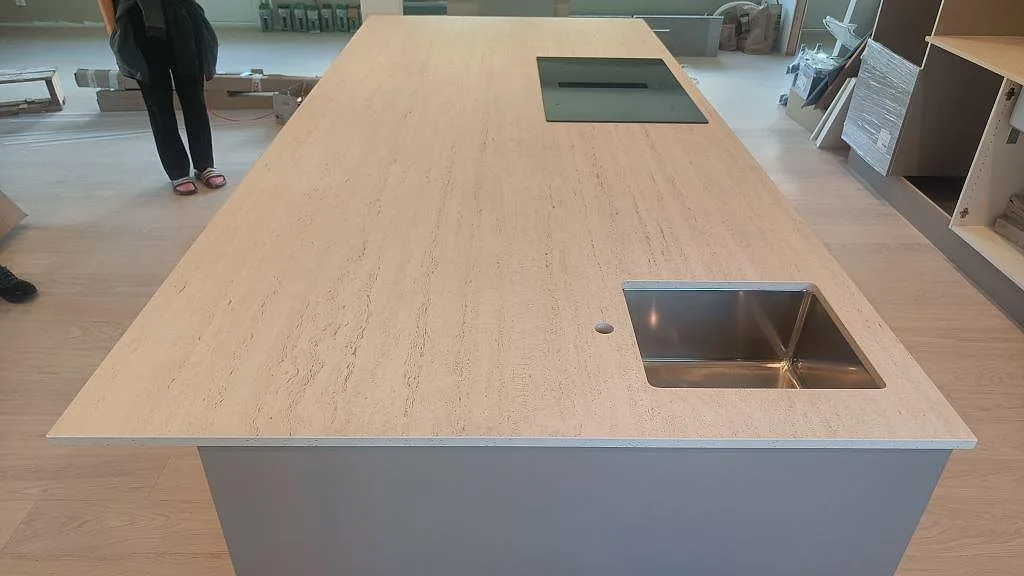 Lång köksö i matt Dekton Marmorio med travertinliknande ådring, underlimmad rostfri diskho och svart häll i Uddevalla.