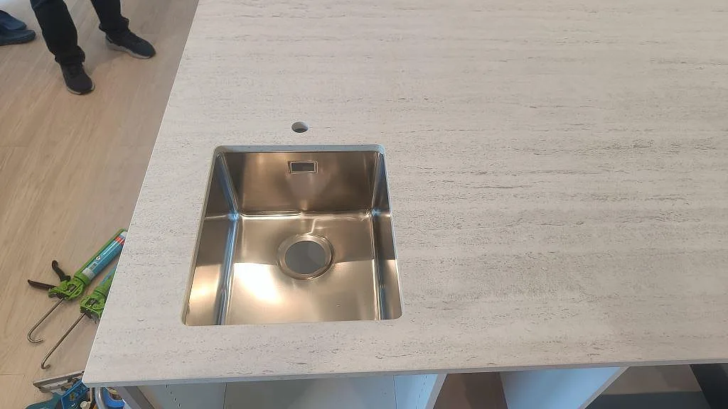 Närbild på underlimmad rostfri diskho i en matt Dekton Marmorio köksbänkskiva med ljus ådring i Uddevalla.
