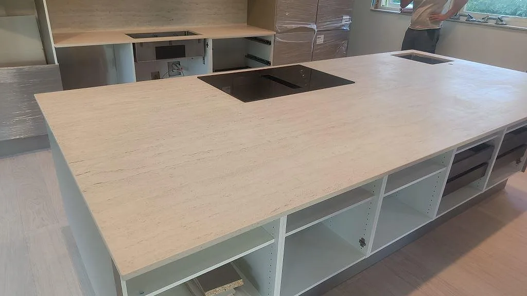 Stor köksö i matt Dekton Marmorio med svart induktionshäll, rostfri diskho och vita köksstommar under montering i Uddevalla.
