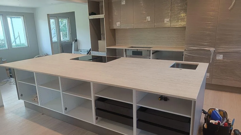 Köksbänkskiva i matt Dekton Marmorio med stor köksö, svart induktionshäll, rostfri diskho och stänkskydd i ett kök i Uddevalla.