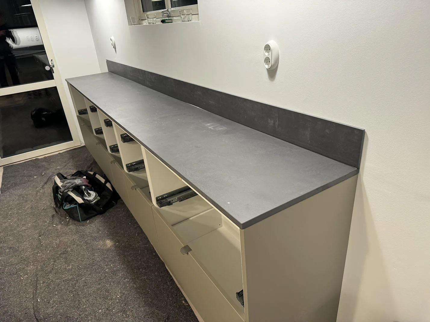 Köksbänkskiva i matt Dekton Micron med lång grå arbetsyta och stänkkant under montering i Olofström.