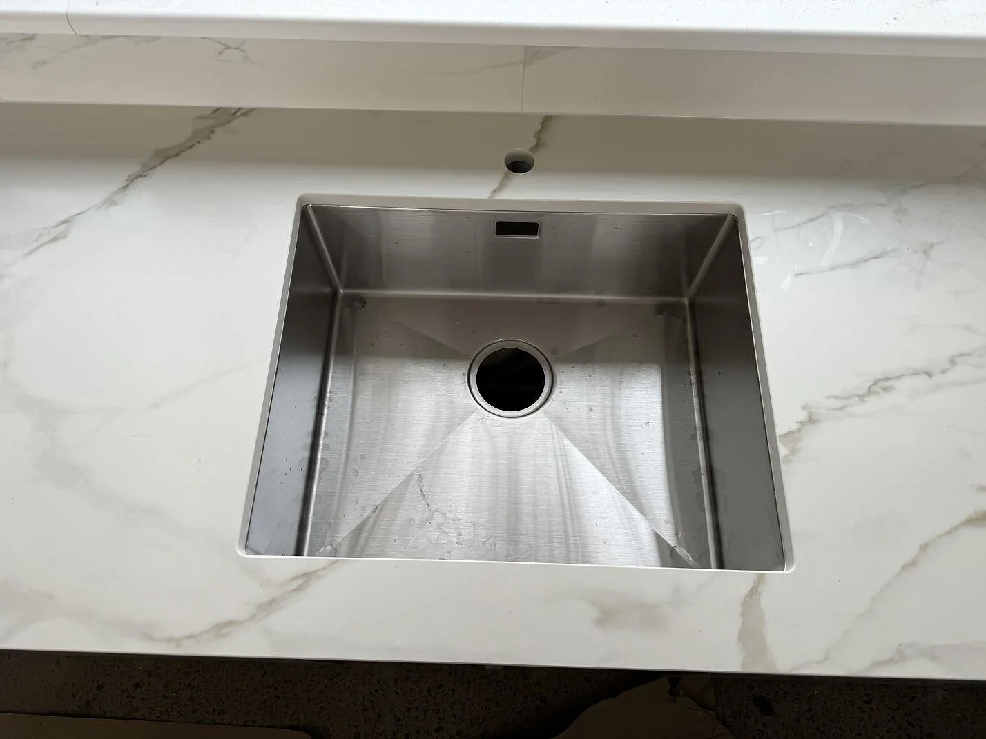 Närbild på underlimmad rostfri diskho i köksbänkskiva av matt Dekton Morpheus Velvet med grå ådring i Billesholm.