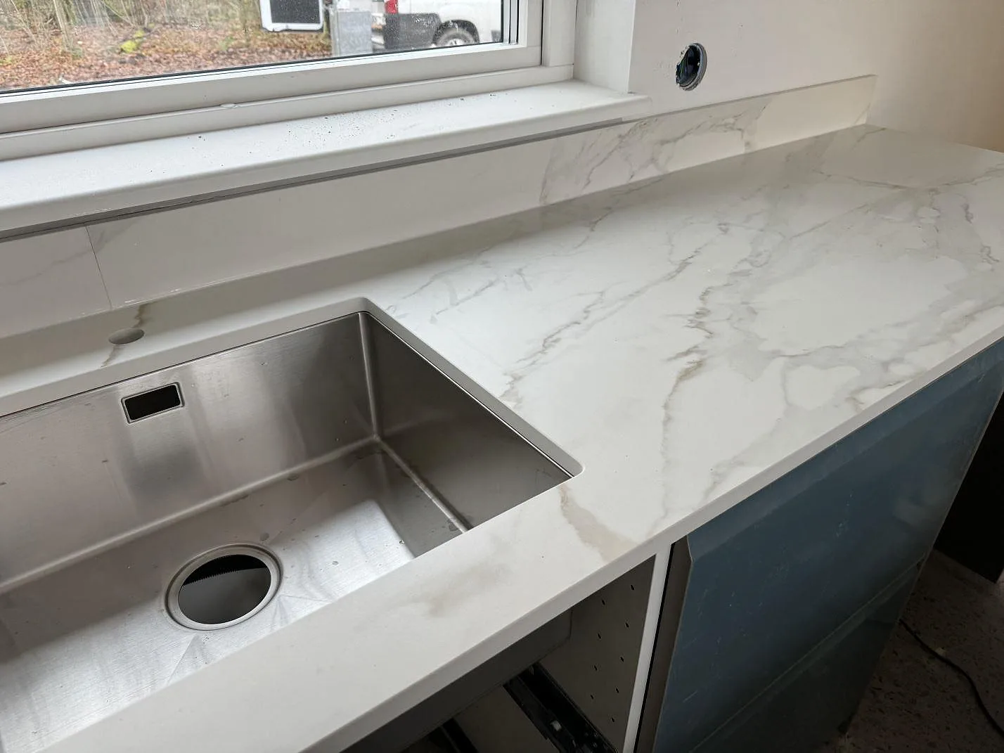 Köksbänkskiva i matt Dekton Morpheus Velvet med underlimmad rostfri diskho, låg stänkkant och blå skåpsinredning i ett kök i Billesholm.