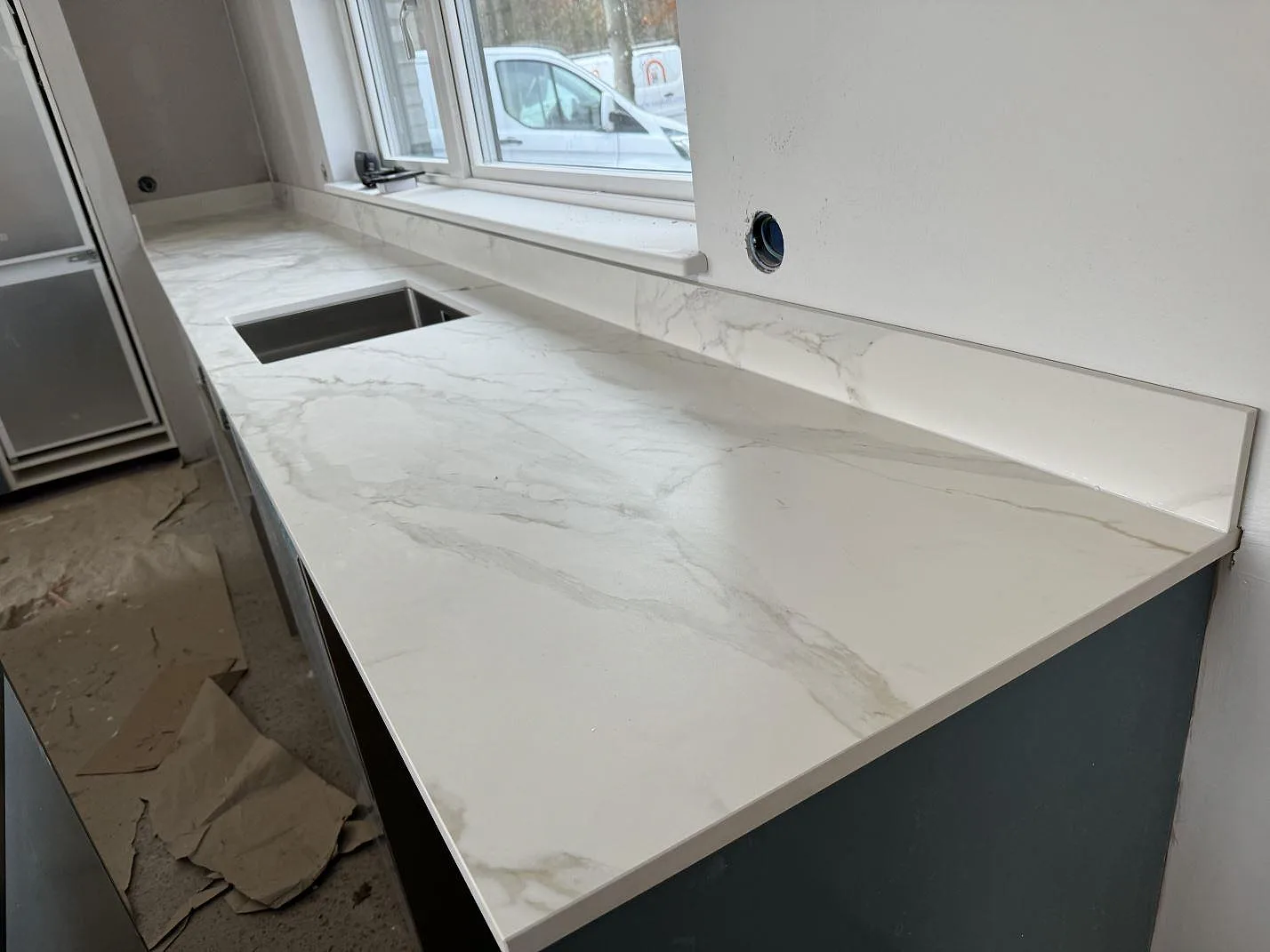 Köksbänk i matt Dekton Morpheus Velvet längs fönstersidan med underlimmad rostfri diskho och ljus ådring i Billesholm.