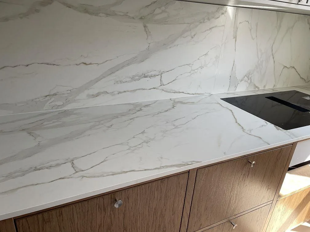 Köksbänkskiva i matt Dekton Morpheus Velvet med tydlig grå och guldgrå ådring som löper genom bänkskiva och stänkskydd i ett kök i Frederiksberg.