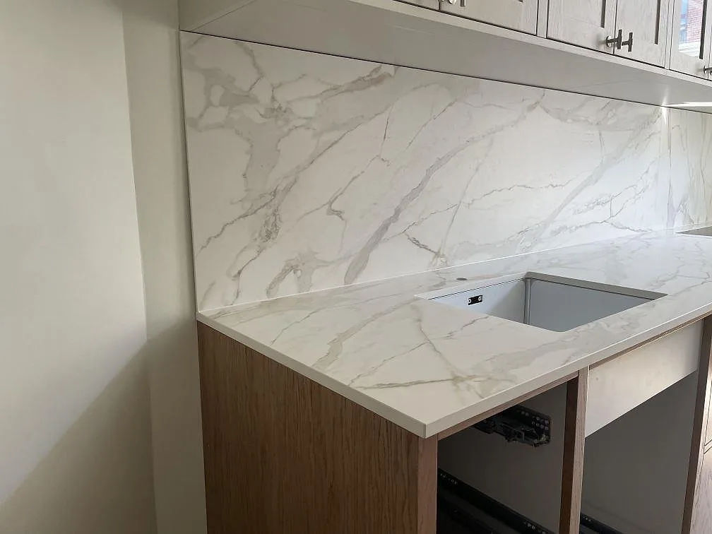 Hörnparti i Dekton Morpheus Velvet, matt keramik med grå ådring, köksbänkskiva med underlimmad diskho och stänkskydd över träluckor i ett kök i Frederiksberg.