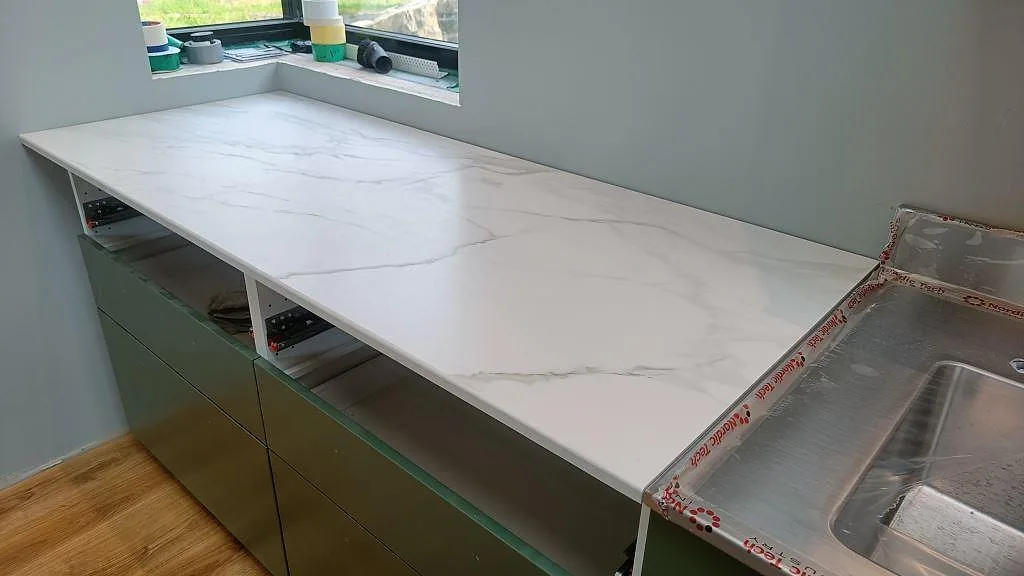 Lång bänkskiva i matt Dekton Morpheus Velvet vid fönster, monterad på salviagröna köksstommar i Kungsbacka.