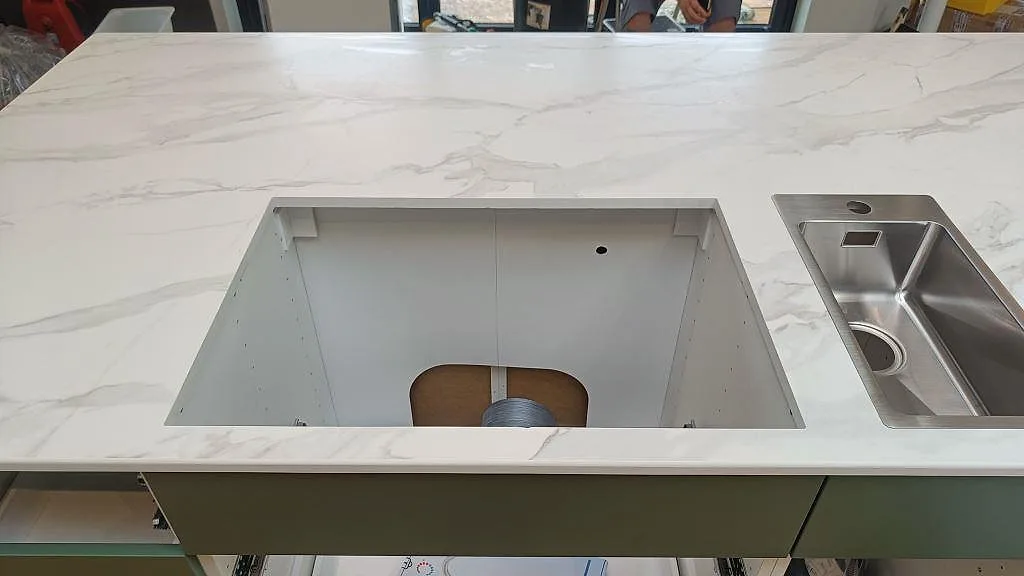 Köksö i vit Dekton Morpheus Velvet keramik med stor utskärning och rostfri diskho under montering i Kungsbacka.