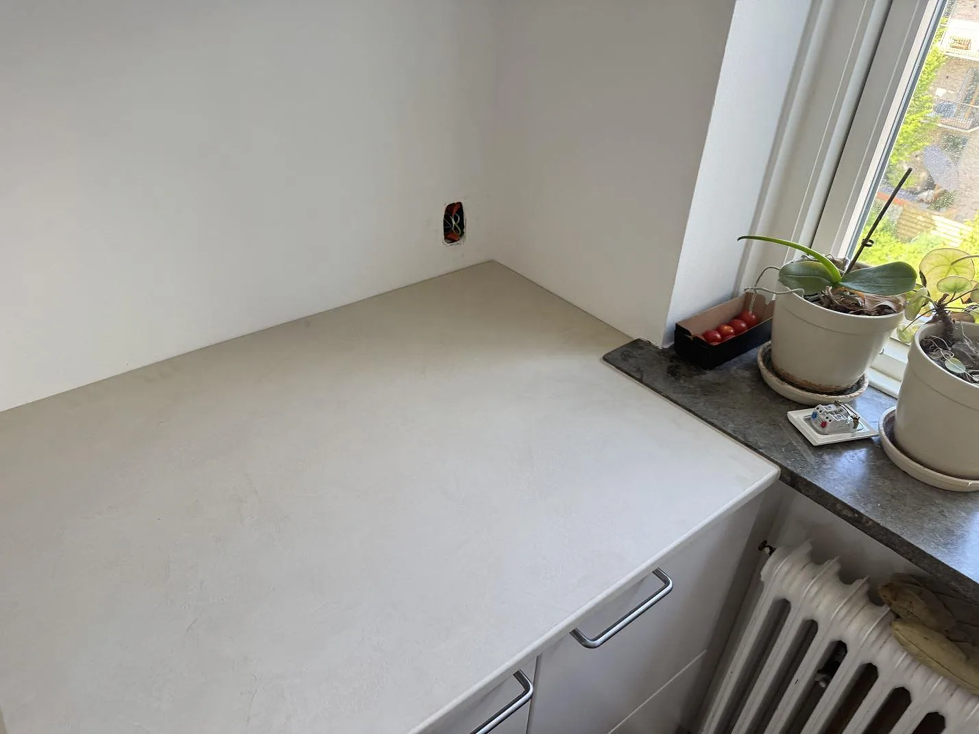 Ljus köksbänkskiva i matt Dekton Nacre Velvet monterad vid fönster och element i ett kök i Frederiksberg.