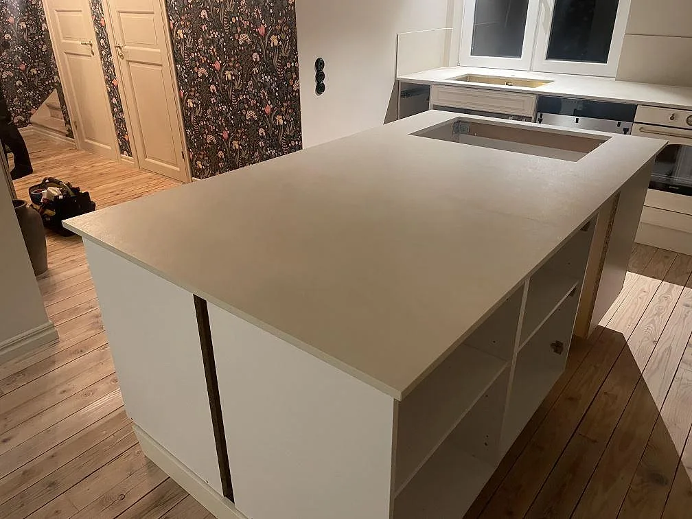 Stor köksö i matt Dekton Nacre Velvet med urtag för häll och bakre bänkskiva med diskho i ett kök i Immeln.