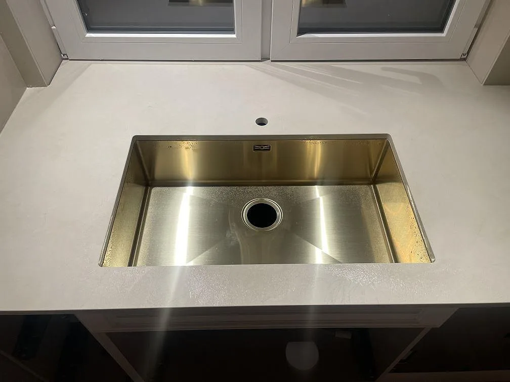 Närbild på rostfri diskho i en bänkskiva av matt Dekton Nacre Velvet med blandarhål under fönster i Immeln.