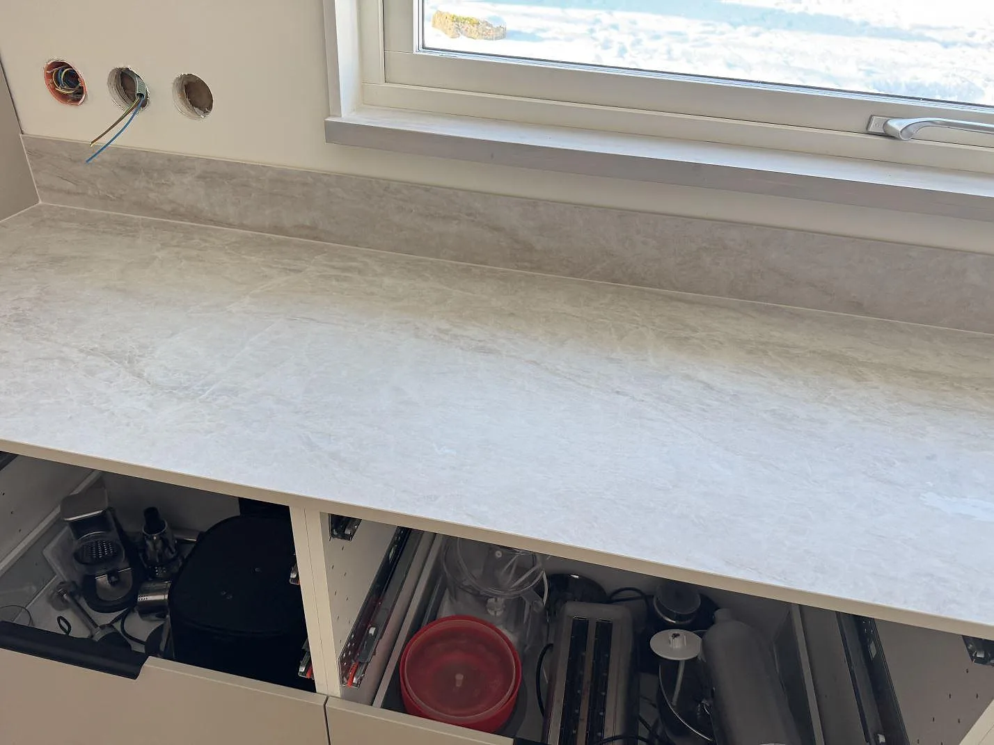 Köksbänkskiva i Dekton Nara, matt keramik, som löper fram till ett fönster med öppna stommar under i ett kök i Fjärås.