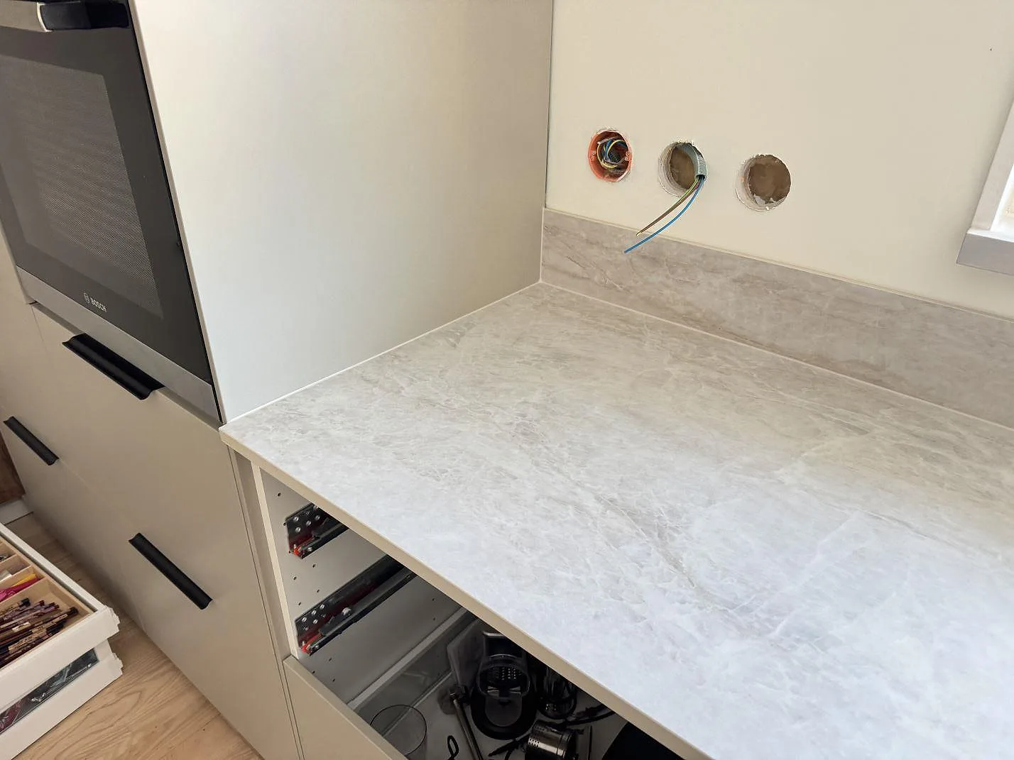 Matt Dekton Nara köksbänkskiva i greige keramik längs en vägg med inbyggd ugn och lågt stänkskydd i ett kök i Fjärås.