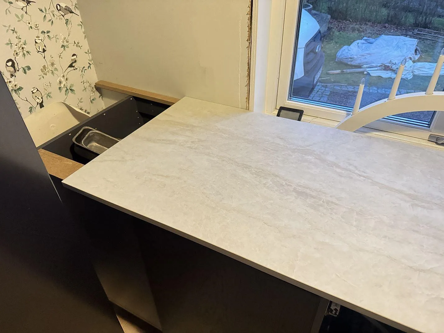Köksbänkskiva i vit Dekton Nara, matt keramik, monterad vid ett fönster med uppvikt stänkkant i ett kök under montering i Halmstad.