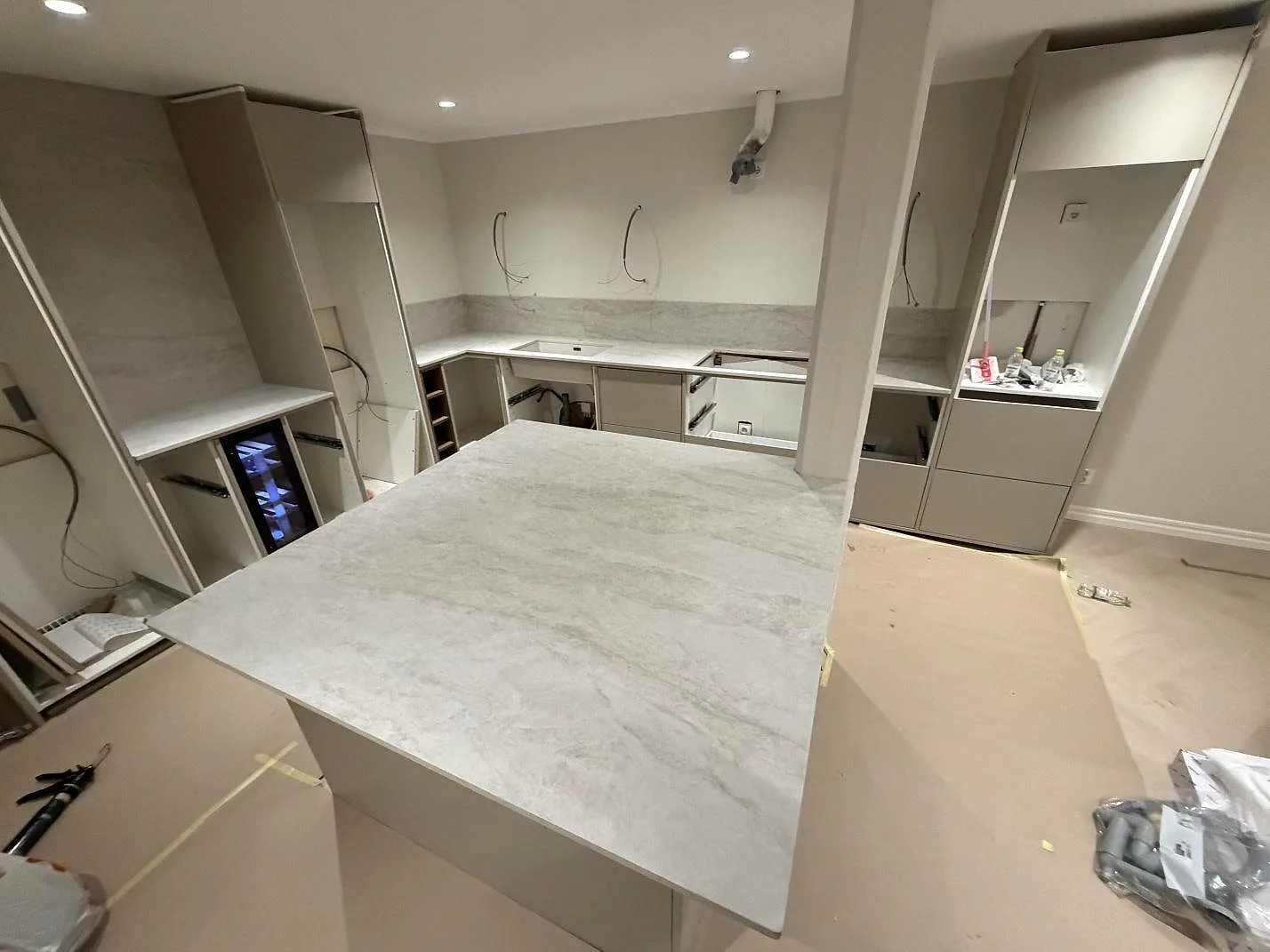 Köksbänkskiva i Dekton Nara, matt offwhite keramik, i ett U-format kök med köksö under montering i Norrköping.
