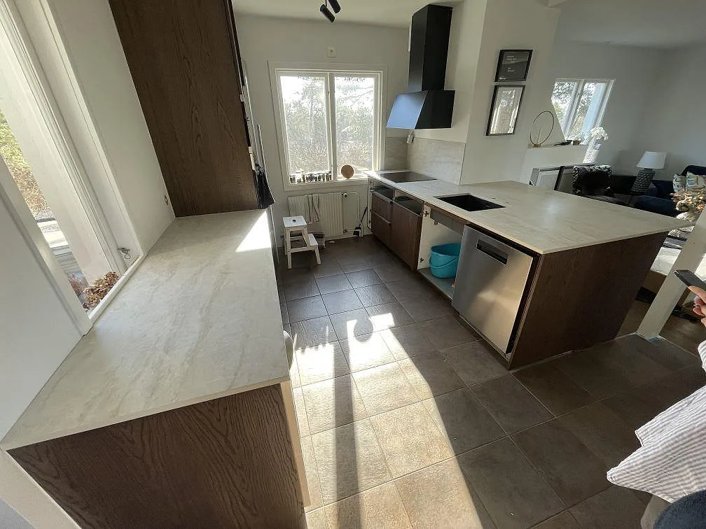 Matt Dekton Nara köksbänkskiva med mörka ekluckor, induktionshäll och rostfri diskmaskin i ett kök i Sollentuna fotograferat innan rummet var helt inrett.