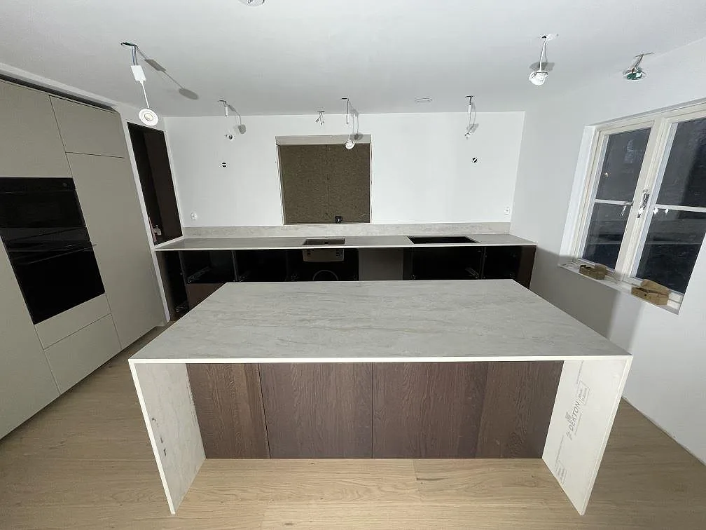 Köksö och köksbänkskiva i matt Dekton Nara, varm offwhite keramik, med gerad kant och urtag för häll i ett kök i Viken.