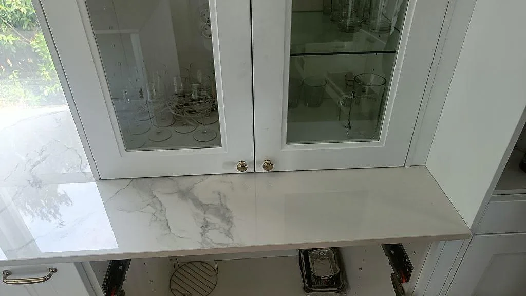 Vit Dekton Natura bänkskiva under vägghängt glasvitrinskåp i ett kök i Karlskrona.