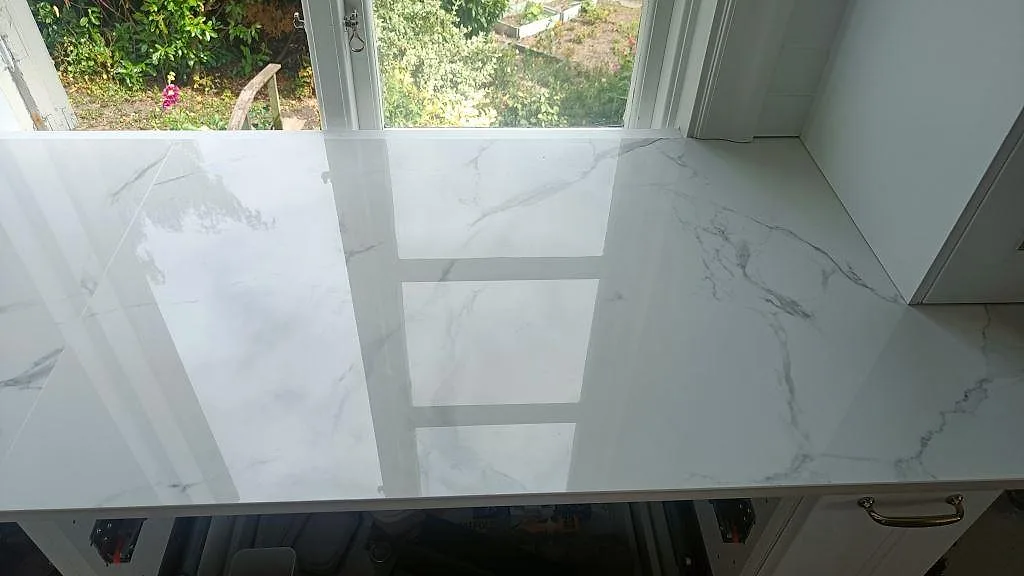 Polerad vit Dekton Natura bänkskiva med mjuk grå ådring vid fönster i ett kök i Karlskrona.