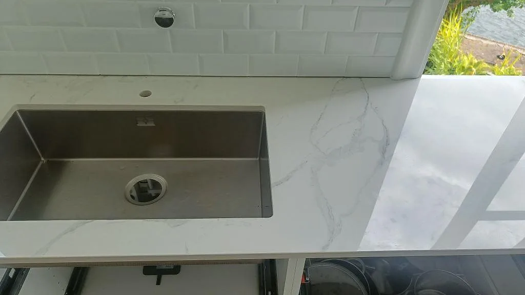 Underlimmad rostfri diskho i vit Dekton Natura köksbänkskiva med vitt tegelkakel i ett kök i Karlskrona.