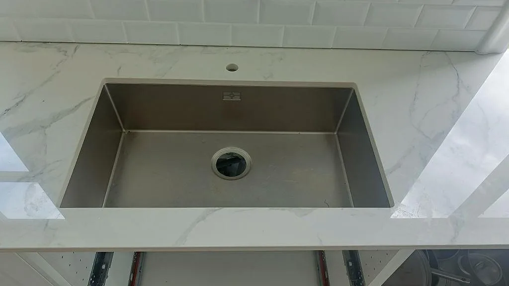 Närbild på underlimmad rostfri diskho i polerad Dekton Natura bänkskiva i ett kök i Karlskrona.