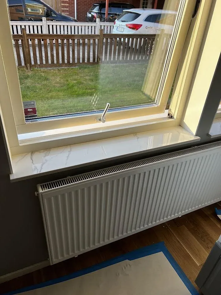 Fönsterbänk i polerad vit Dekton Natura med grå ådring ovanför radiator i ett kök i Landskrona.