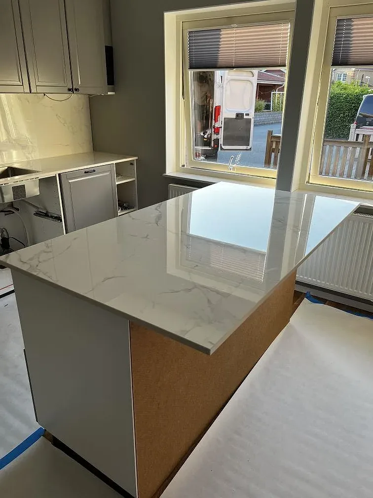 Polerad Dekton Natura köksö med marmorlik ådring, trätonad sida och stora fönster i ett kök i Landskrona.