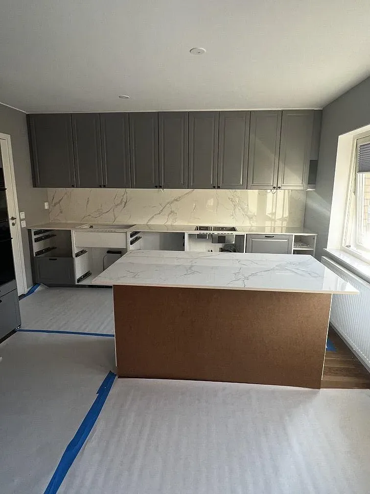 Köksbänkskiva och köksö i polerad vit Dekton Natura keramik med grå ådring i ett kök under montering i Landskrona.