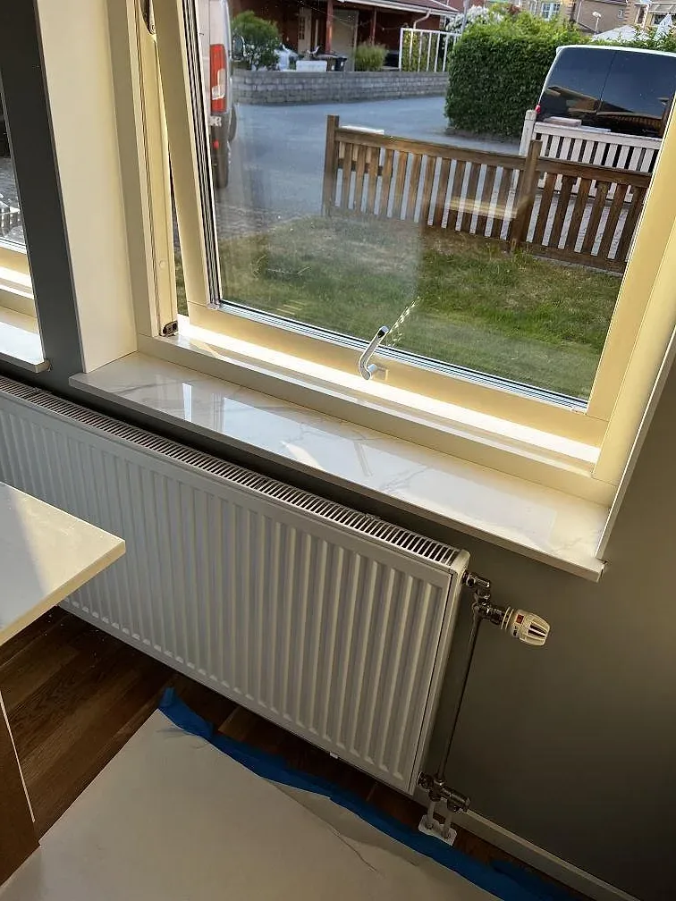 Detalj av fönsterbänk i polerad Dekton Natura keramik med ljus reflektion vid stora fönster i Landskrona.