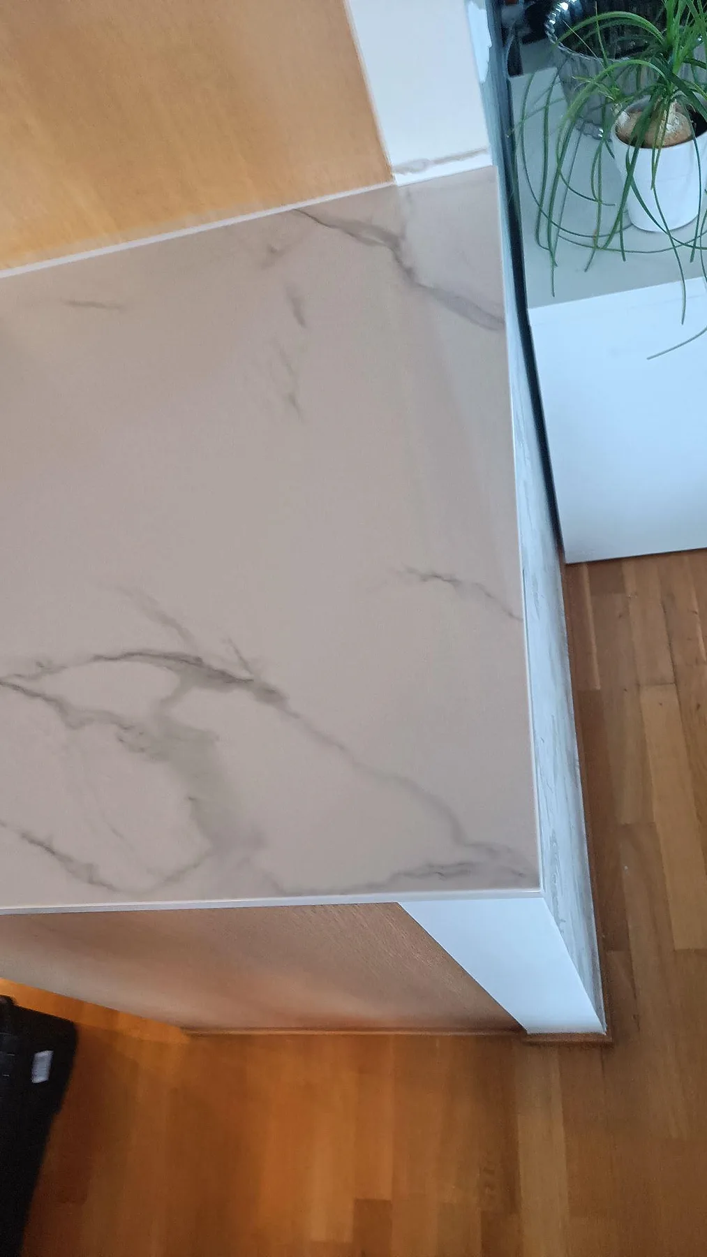 Detalj av polerad Dekton Natura bänkskiva vid vägg och träskiva, med grå ådring och blank yta i Limhamn.